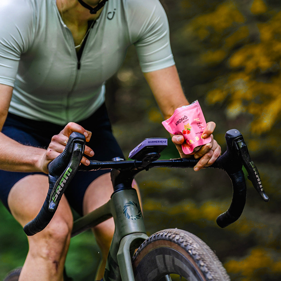 Person riding a bicycle holding a pink energy gel with a blurred natural background