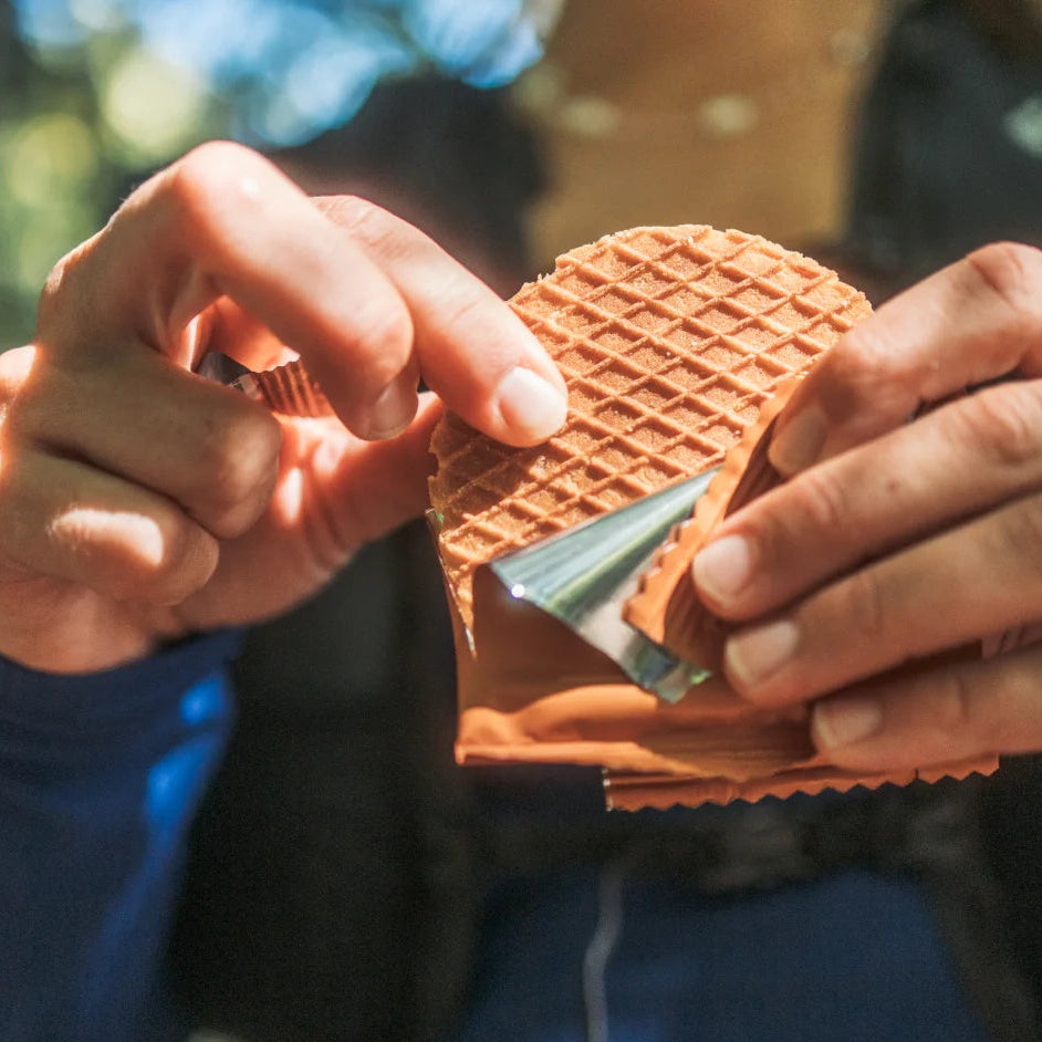 A close-up lifestyle shot of a person's hands holding a waffle cone filled with orange custard or ice cream, wearing a blue long-sleeve shirt.