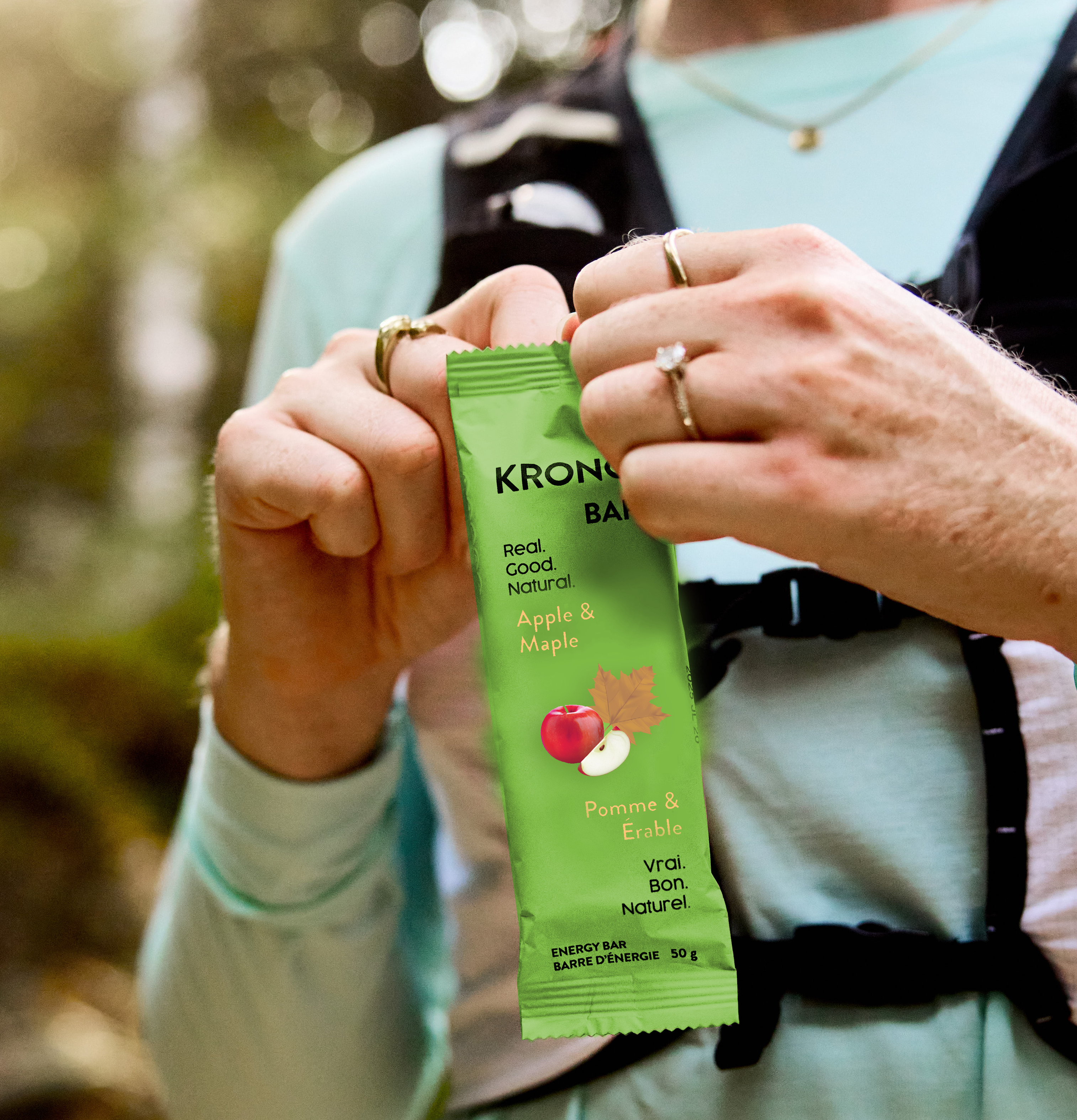 Trail runner opening a Krono Nutrition maple and apple energy bar, with a blurry forest in the background