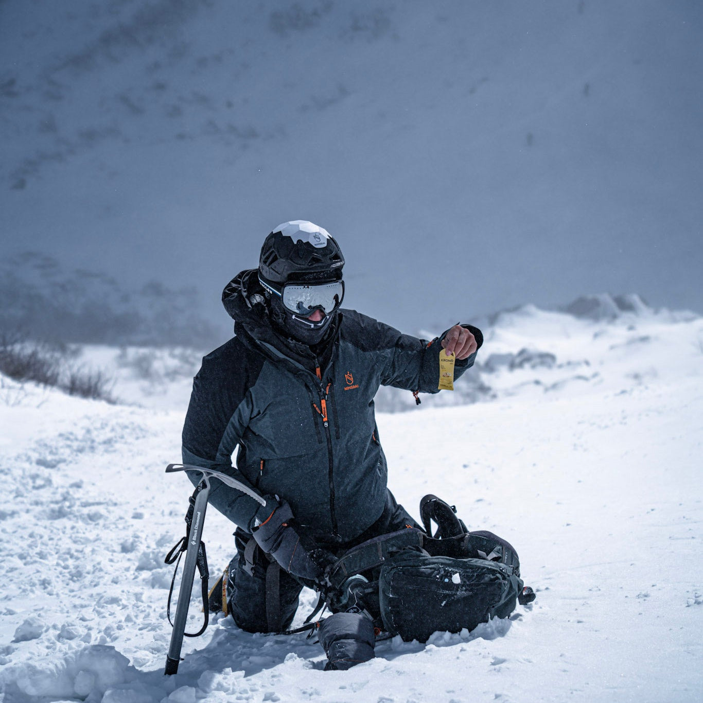 Winter hiker holding a Krono Nutrition citrus fruits energy gel while taking a break from climbing the snowy mountain