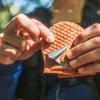A close-up lifestyle shot of a person's hands holding a waffle cone filled with orange custard or ice cream, wearing a blue long-sleeve shirt.