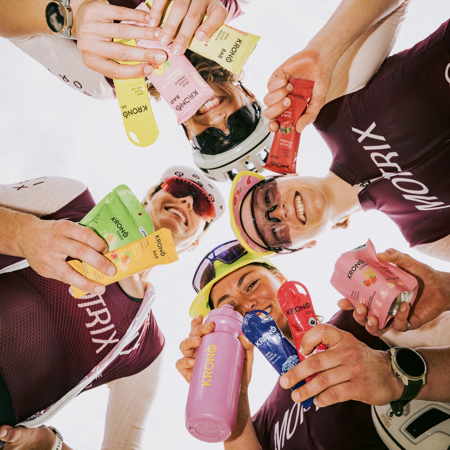 Cyclists holding every type of products offered by Krono Nutrition, in a circle, looking down to the camera