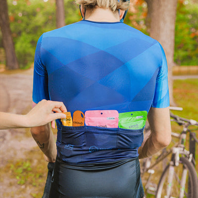 Person wearing a blue cycling jersey with pockets on the back filled with Krono Nutrition bars, gels and chews