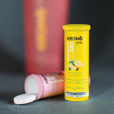 Krono Nutrition lemon and lime effervescent tablets standing, with a pink lemonade tube laying down next to one of its tablets, on a countertop