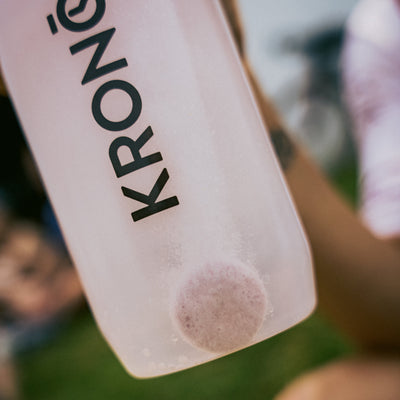 Runner mixing a Krono Nutrition pink lemonade effervescent tablet in his water bottle, outdoors