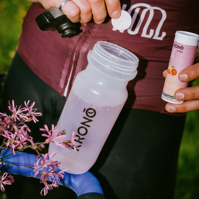 Cyclist about to put a Krono Nutrition pink lemonade effervescent tablet in his water bottle, while holding the tube with his other hand