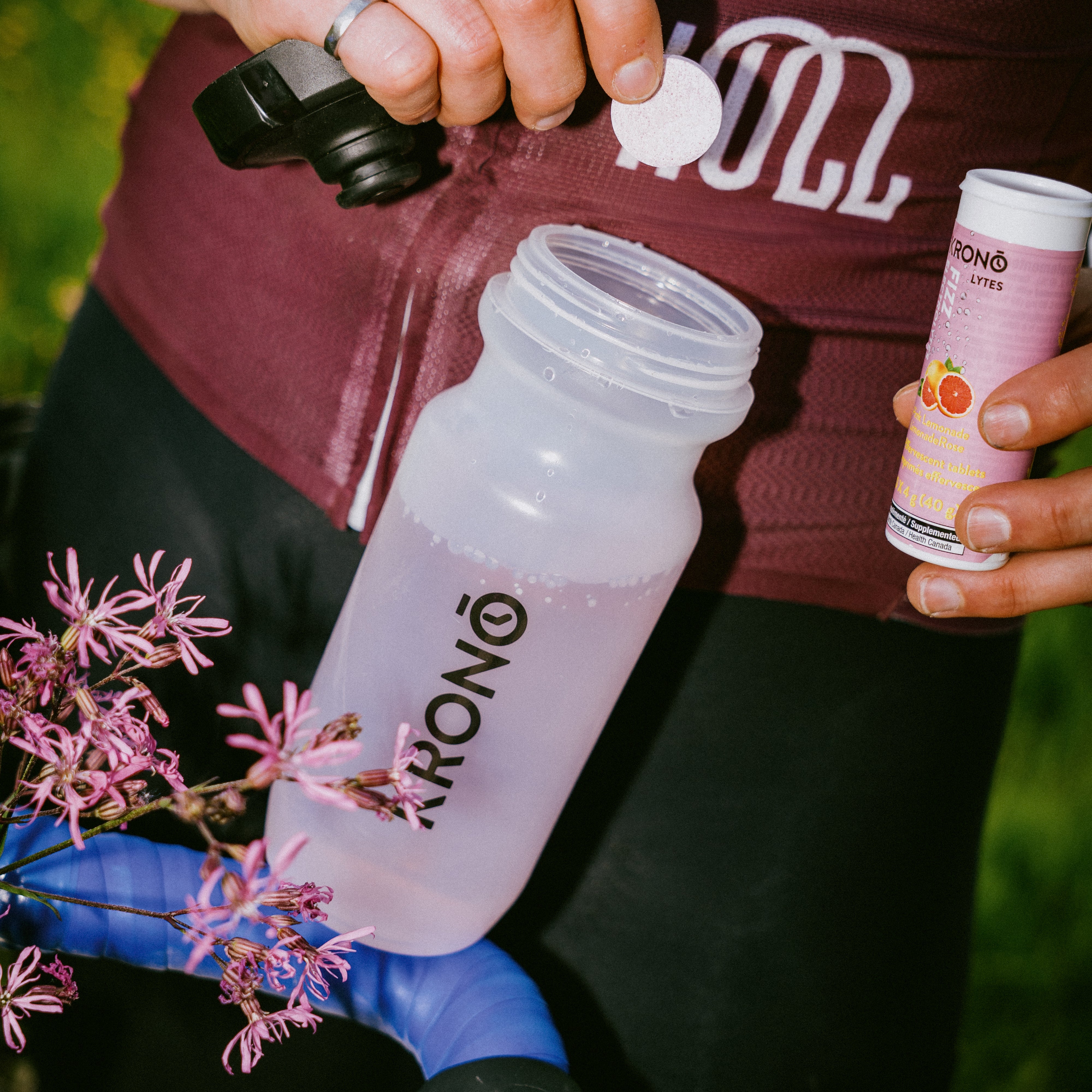 Cyclist about to put a Krono Nutrition pink lemonade effervescent tablet in his water bottle, while holding the tube with his other hand