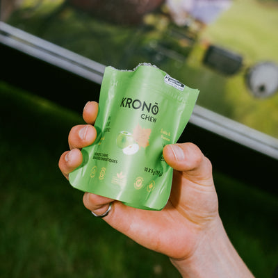Person holding a Krono Nutrition maple and apple energetic chews bag, outdoors with a blurry grass background