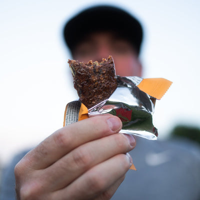 Close-up of runner holding a Krono Nutrition apricot and cranberry energy bar, outdoors