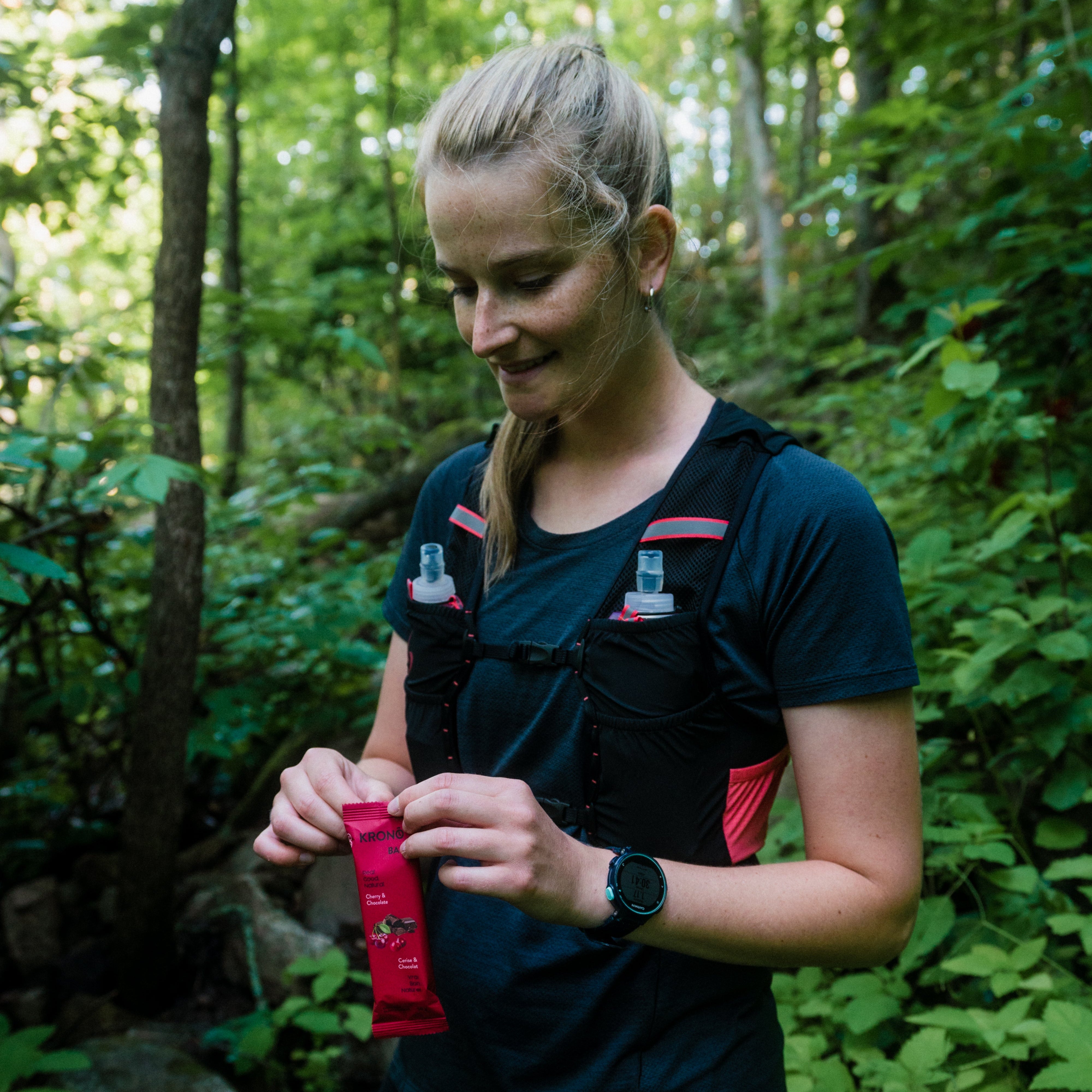 Trail runner opening Krono Nutrition cherry and chocolate energy bar, on a trail