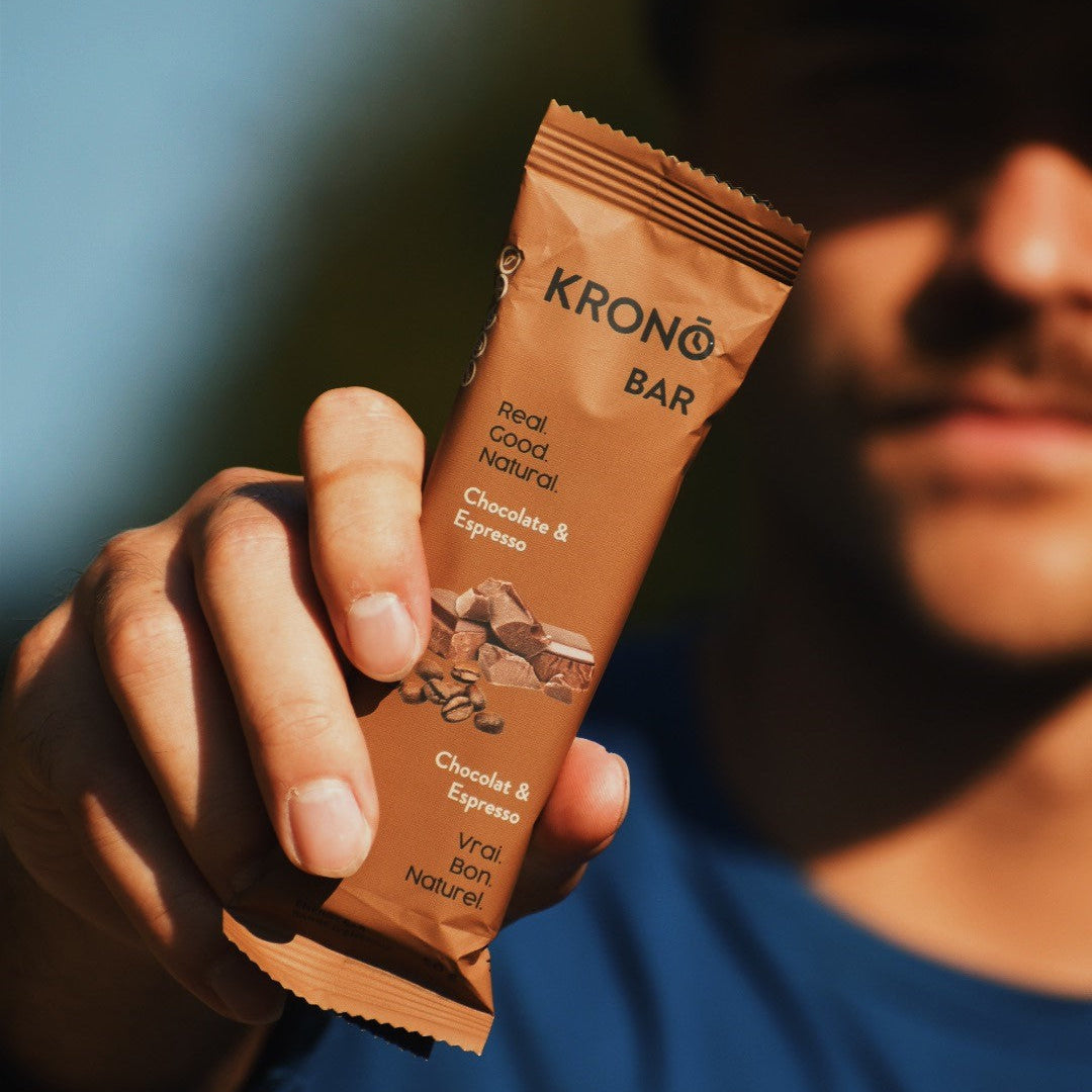 Close-up of runner holding a Krono Nutrition chocolate and espresso energy bar, outdoors