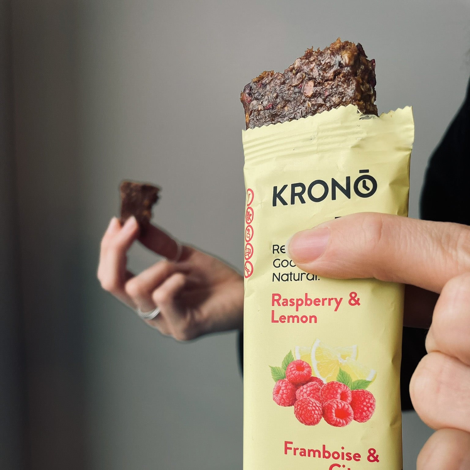 Close-up of person holding a Krono Nutrition raspberry and lemon energy bar while eating a piece