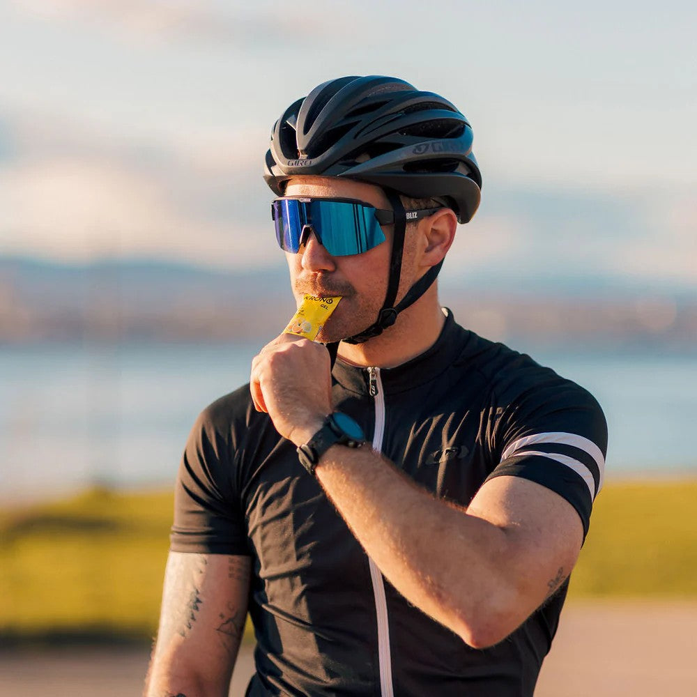 Cyclist drinking a Krono Nutrition citrus fruits energy gel, with a blurry outdoors background