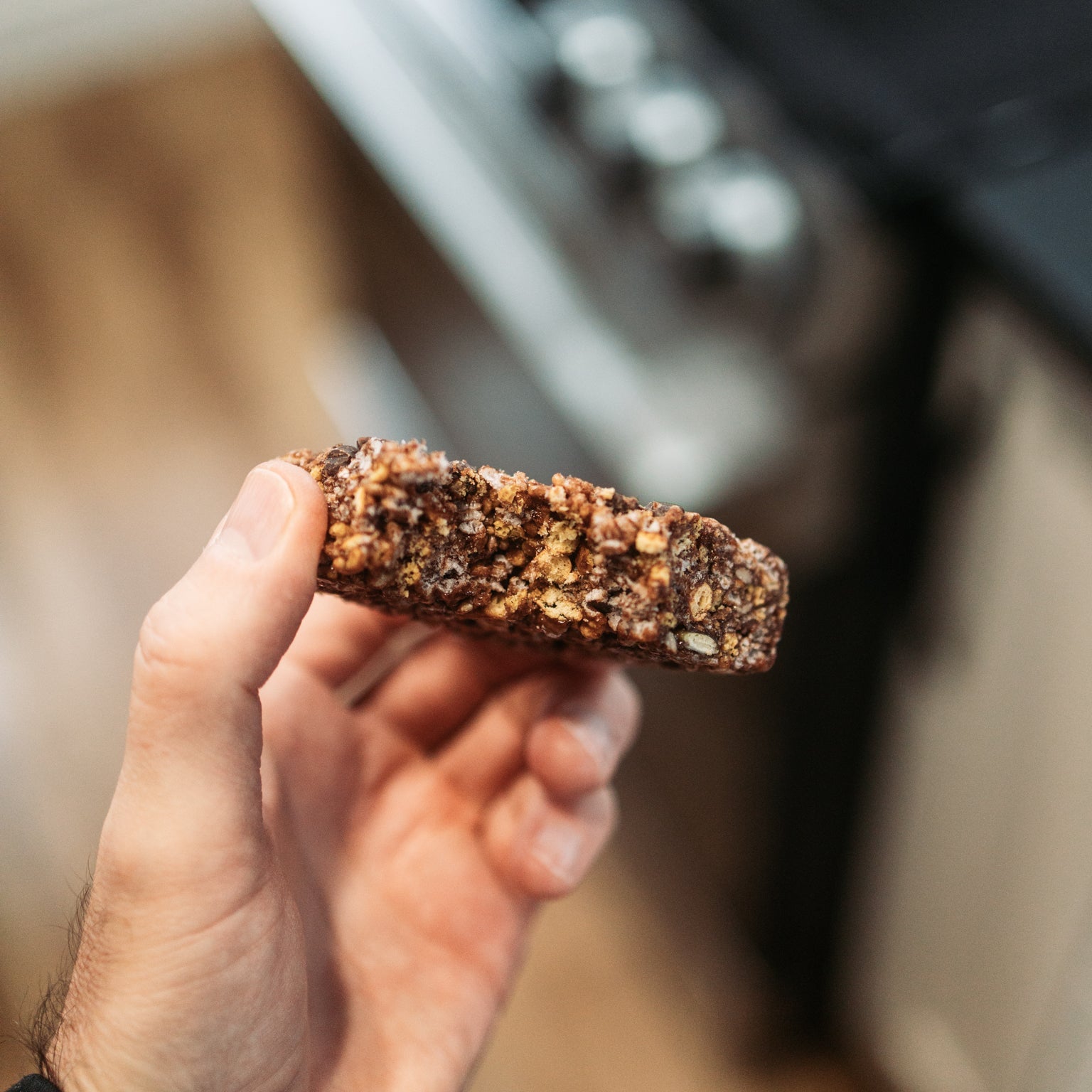Close-up of a Krono Nutrition pretzel and chocolate energy rice cake, with a bite taken out of it, being held by a person, with a blurry background