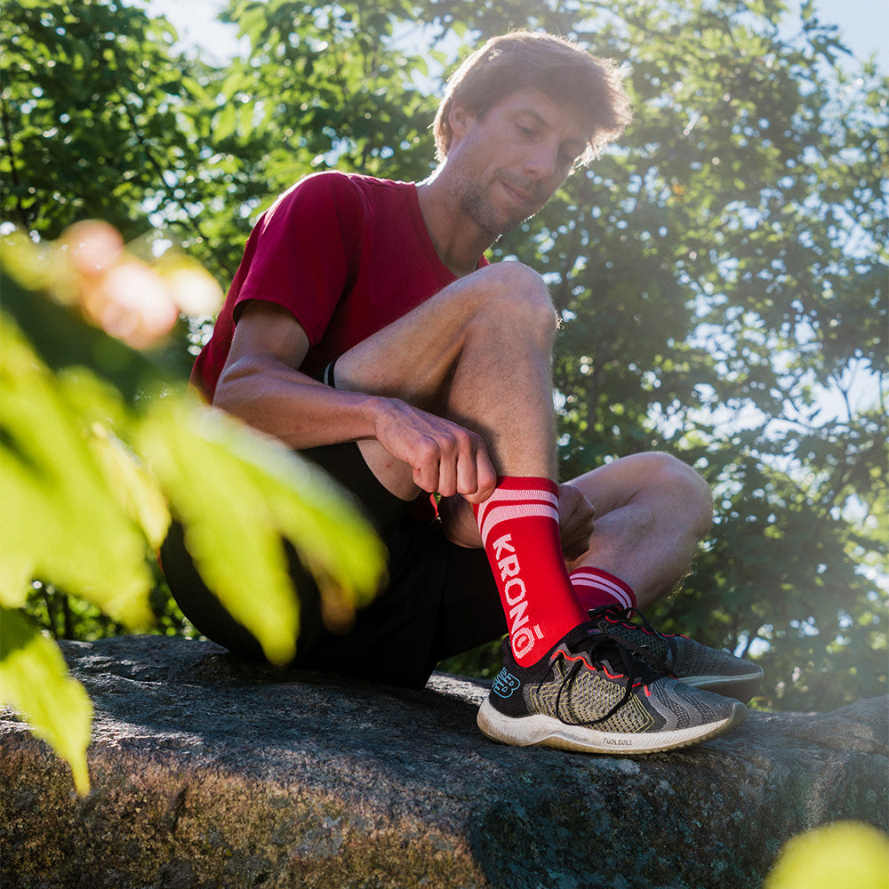 Runner adjusting his Krono Nutrition socks vintage OUTWAY, cherry, on a trail