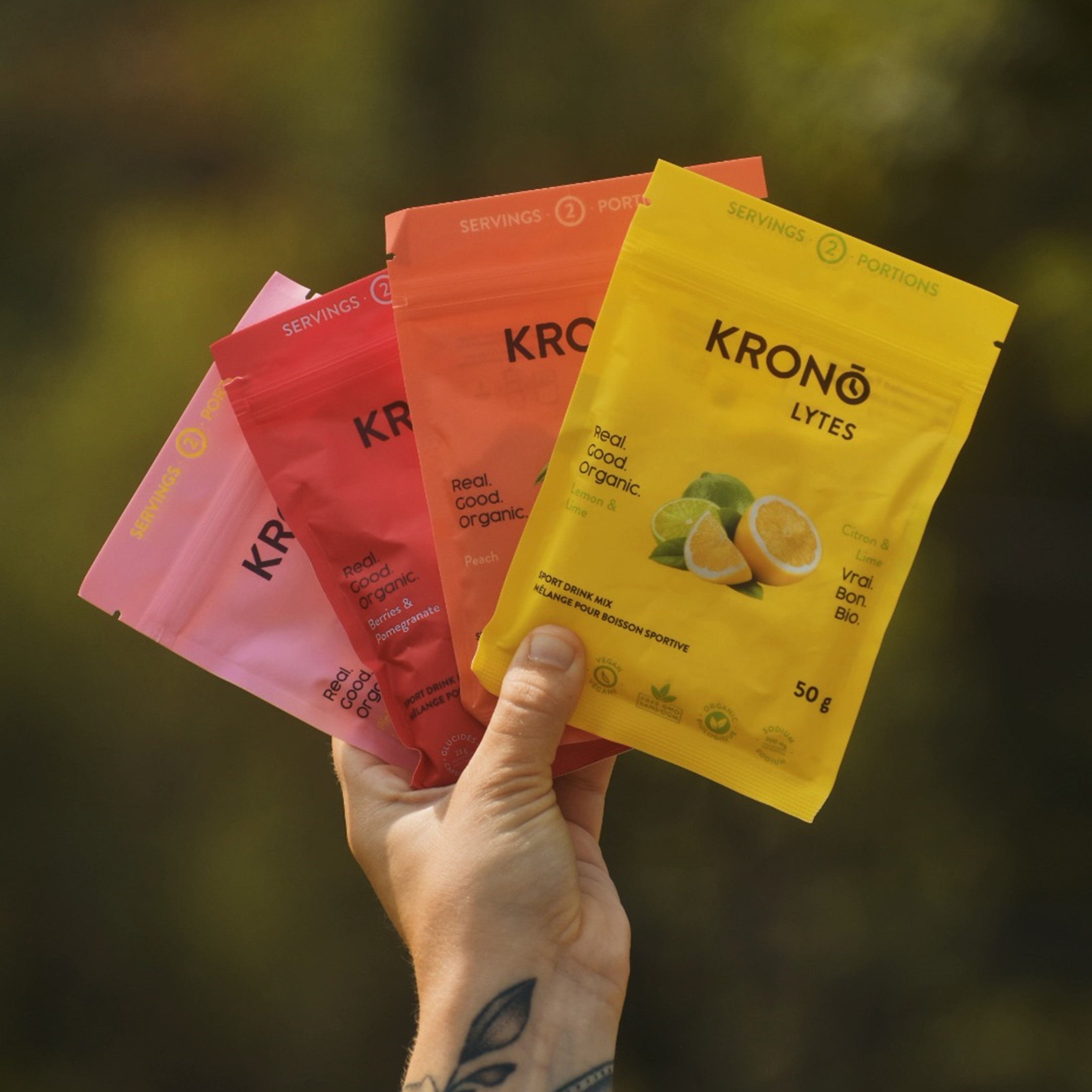 Close-up of runner holding all four Krono Nutrition variety pack sport drink mixes, outdoors