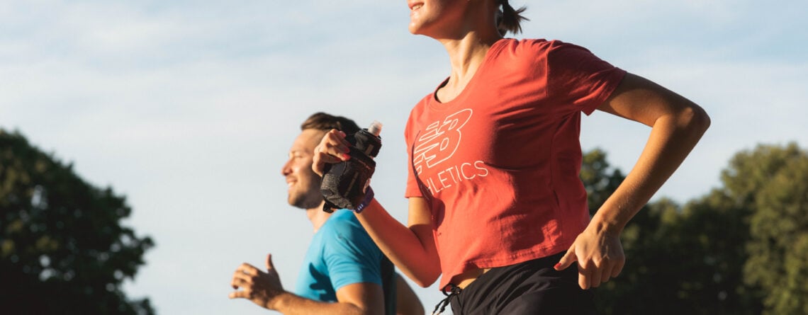 Une femme et un homme courent côte à côte avec énergie, vêtus de short et t-shirt, à l'extérieur sous un ciel bleu