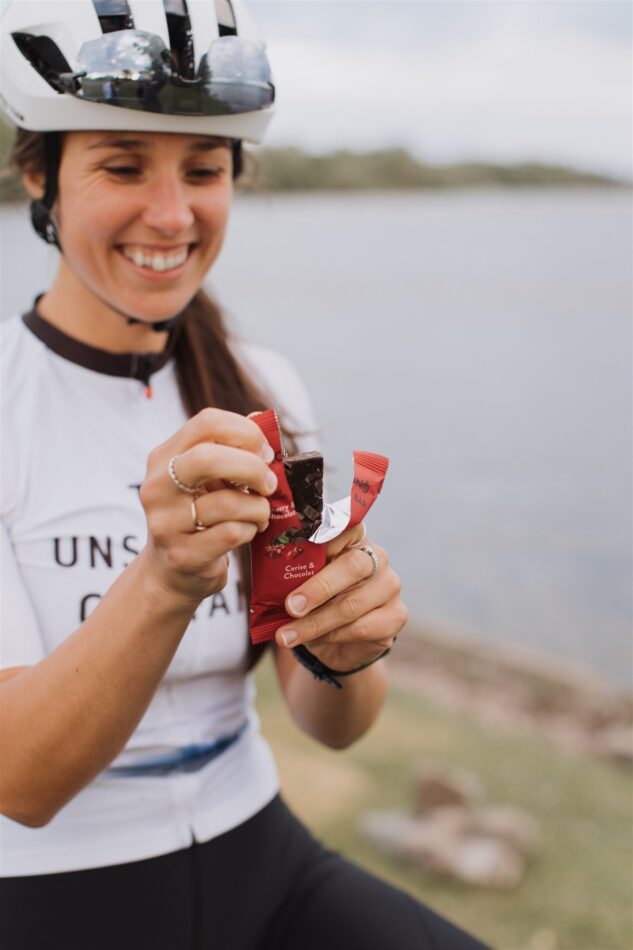 Femme cycliste consommant une barre énergétique Krono, devant un lac.