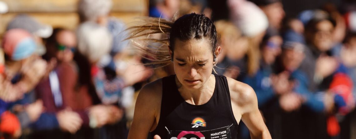 Athlète féminine courant un marathon en été, passant devant des spectateurs.