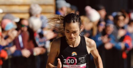 Athlète féminine courant un marathon en été, passant devant des spectateurs.