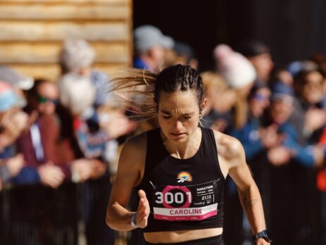 Athlète féminine courant un marathon en été, passant devant des spectateurs.