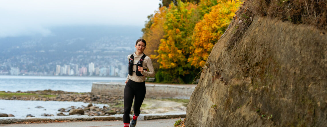 Athlète féminine de course à pied courant sur une route urbaine au bord de l'eau, en automne.