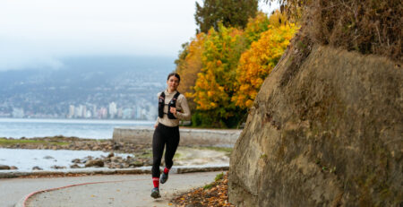 Athlète féminine de course à pied courant sur une route urbaine au bord de l'eau, en automne.