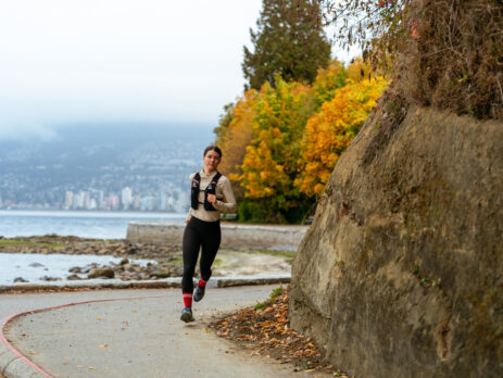 Athlète féminine de course à pied courant sur une route urbaine au bord de l'eau, en automne.