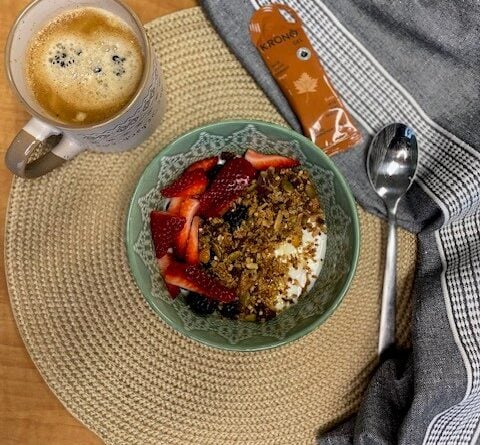 Bol granola, café et Krono Gel à l'érable, sur un napperon rond et accompagnés d'une cuillère et d'une serviette de table.