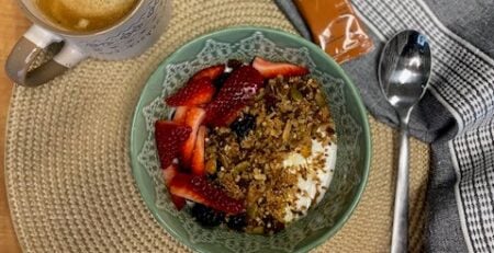 Bol granola, café et Krono Gel à l'érable, sur un napperon rond et accompagnés d'une cuillère et d'une serviette de table.