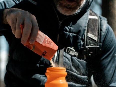 Homme assis qui verse un mélange d'électrolytes Krono Lytes dans une bouteille d'eau.