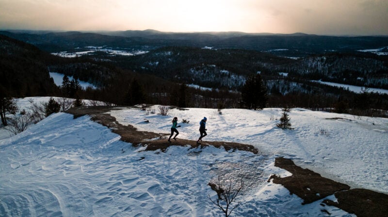 Homme et femme courant au sommet d'une montagne enneigée.